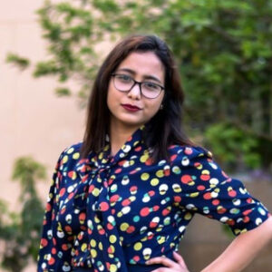 Sampreeti Bhattacharya wearing a polka dot shirt and standing with her hand on her hip.