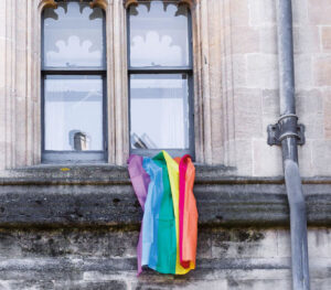 Image of rainbow flag hanging out of window of Victorian-style academic building.